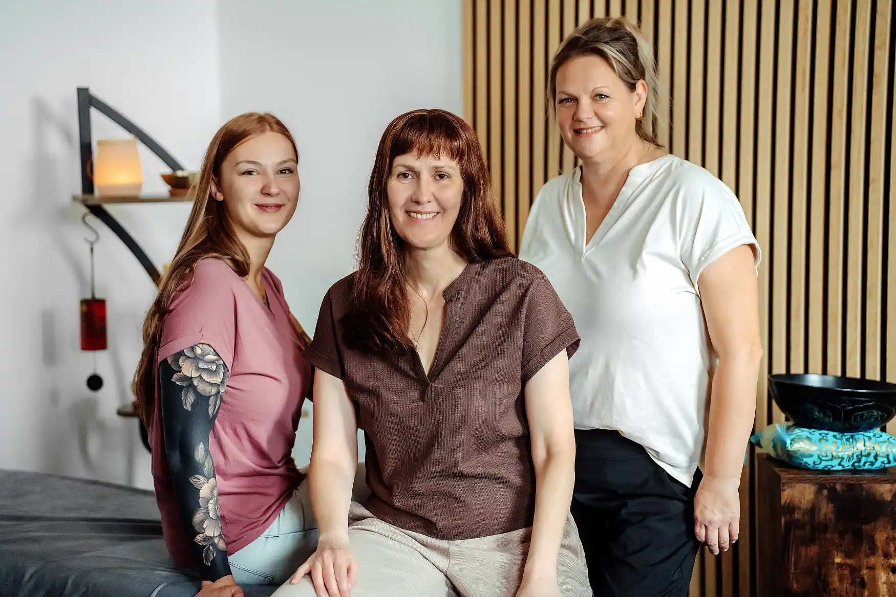 Freundliches Team von drei Frauen, die auf einem bequemen Sofa in einem modernen Büro sitzen und das Buchregal im Hintergrund zeigt.